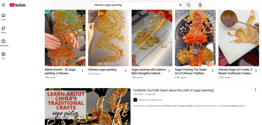YouTube搜索chinese sugar painting的结果页，糖画相关视频播放量从2200到21万不等，其中最高的糖画大师视频21万播放，中国传统甜蜜艺术6500播放，天宇文化的糖画工艺介绍视频5年前发布2600播放